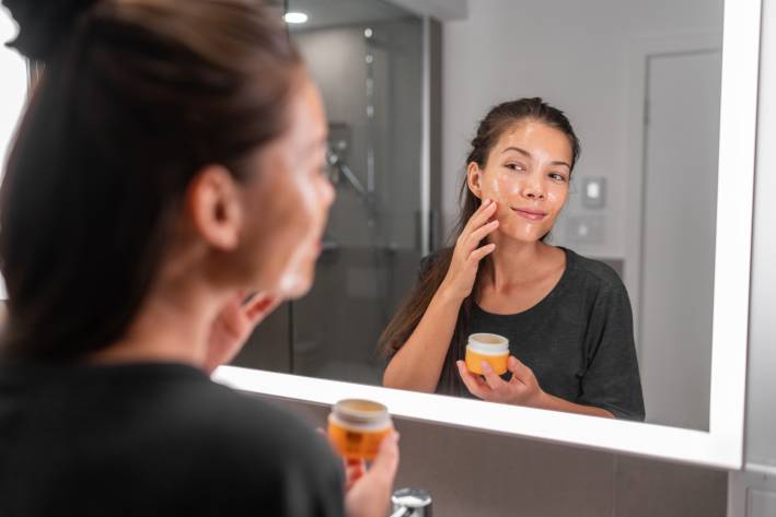 Manuka Honey A woman adding honey to her skin in front of a bathroom mirror.