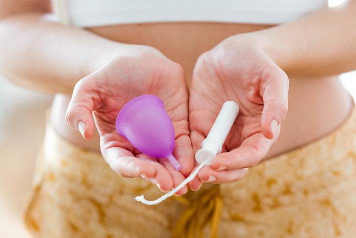 a woman holding a menstrual cup and a tampon