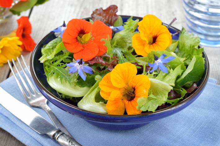 a bowl of salad topped with nasturtiums and borage