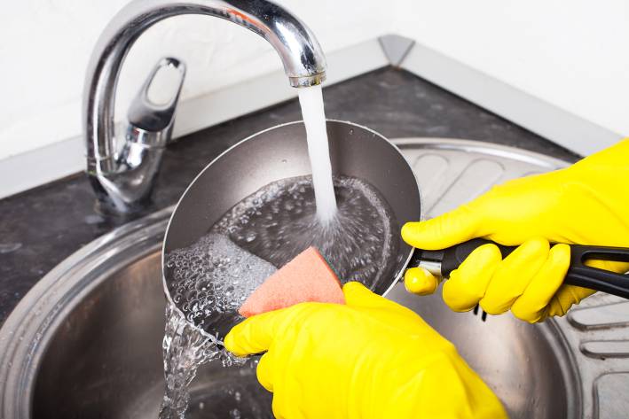 scrubbing a frying pan under hot water
