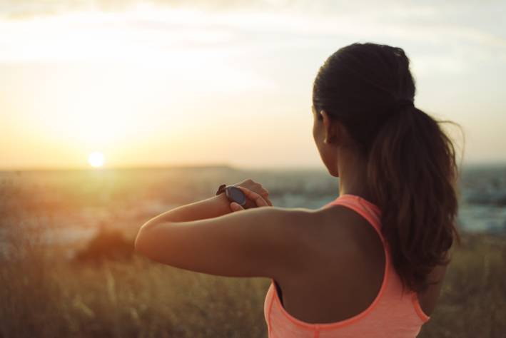 Woman checking workout goals on smart watch looking towards the sunset.