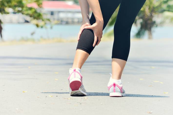 Woman holding calf during a muscle spasm while running.