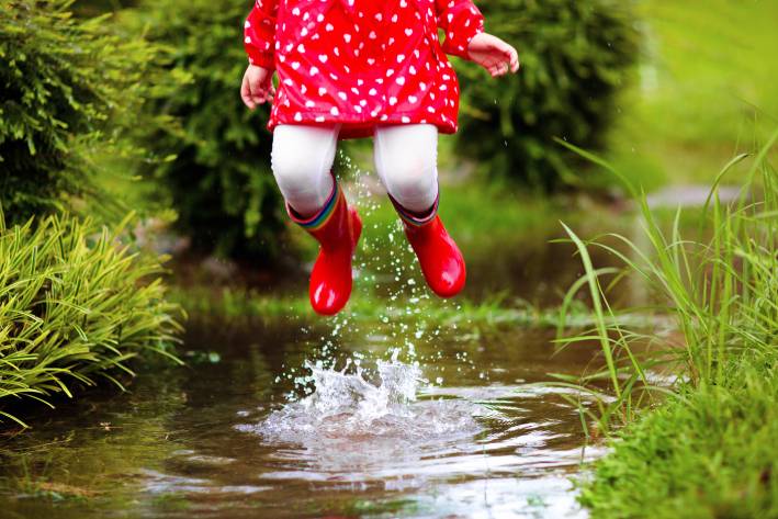 Natural Movement Young girl with red rubber boots jumping up from a creek.
