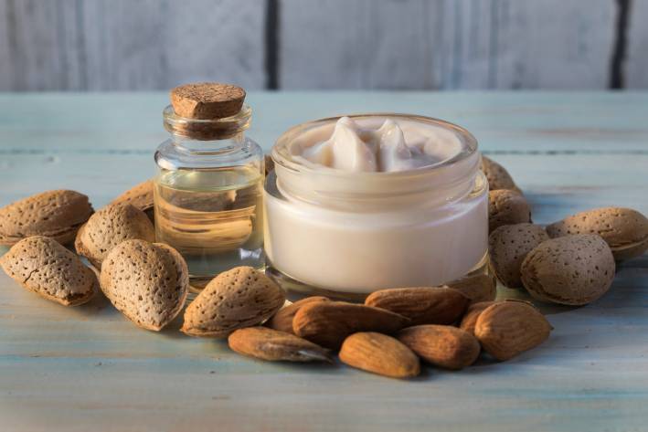 Hand cream and almond oil surrounded by natural almonds