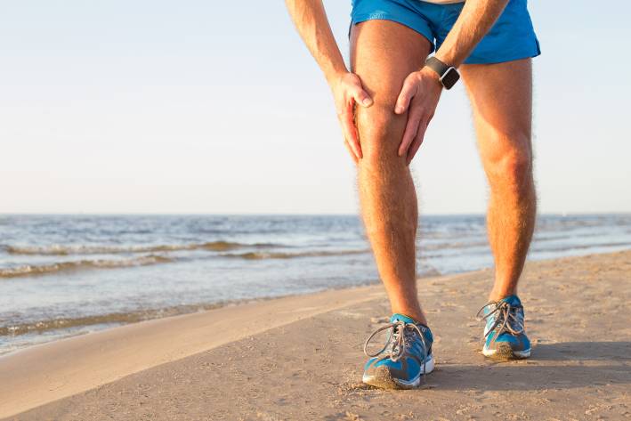 A man with an aching knee while running on the beach