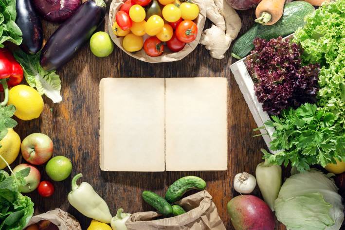 A blank notebook on a rustic table surrounded by fruits and vegetables.