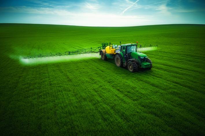 a tractor driving through a field of crops spraying