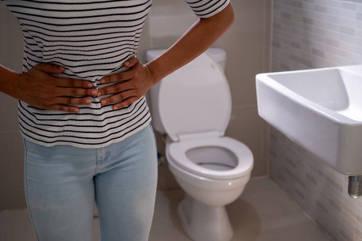 a woman holding her bladder area in pain, near a toilet