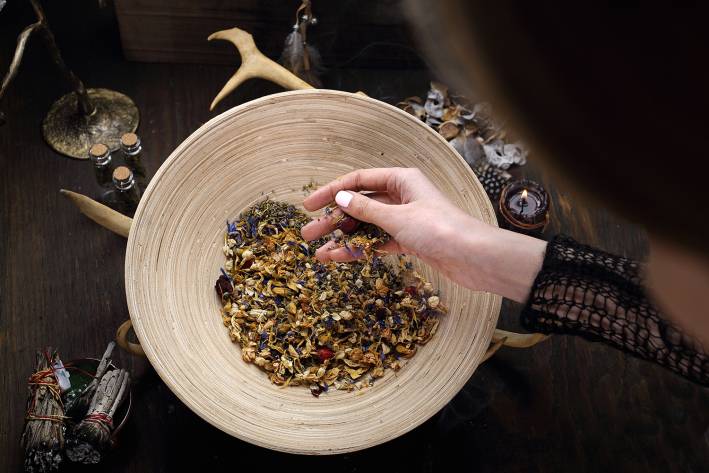 a woman mixing medicinal herbs near a smudge stick and a candle