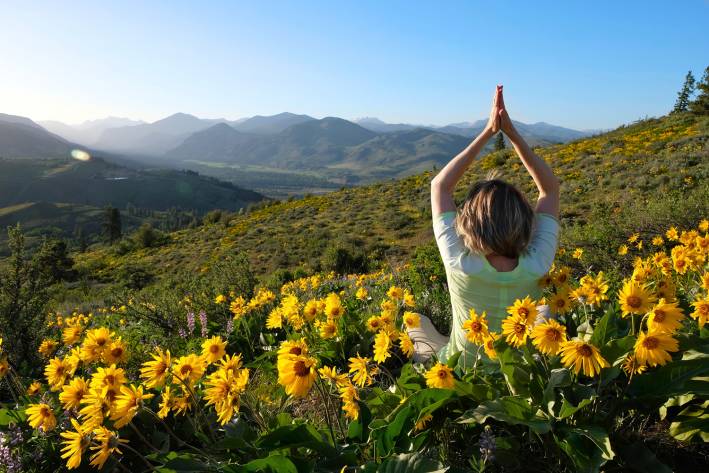 A woman doing yoga, overlooking the mountains in an Arnica field.