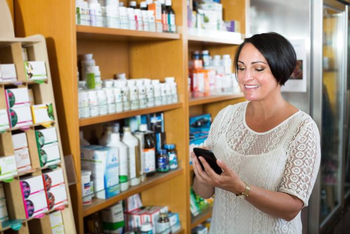 A woman looking up info on her phone while choosing a probiotic supplement.