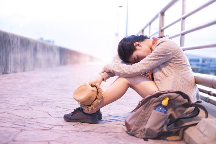 An exhausted woman sitting against a railing with her head on her knees