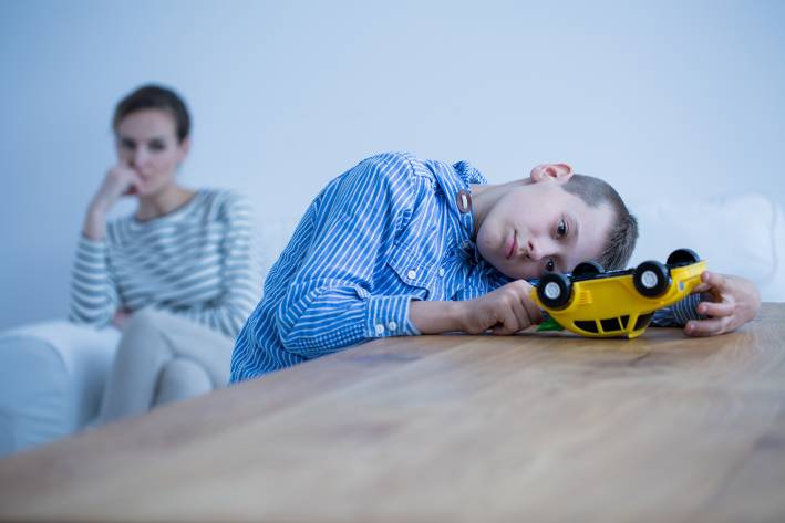 An autistic boy playing with a truck while his mother watches