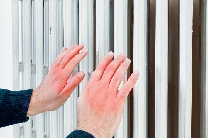 a frostbitten man warming his hands near a radiator