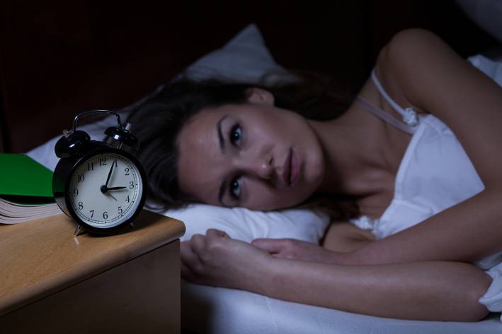 a woman laying awake in bed staring at her alarm clock