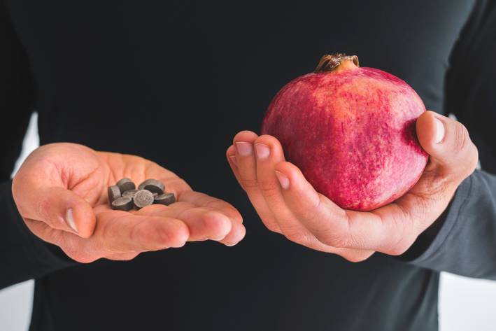 a man holding iron supplements and a pomegranate