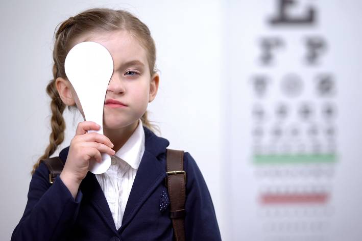 a little girl covering one eye during an exam at the optometrist's