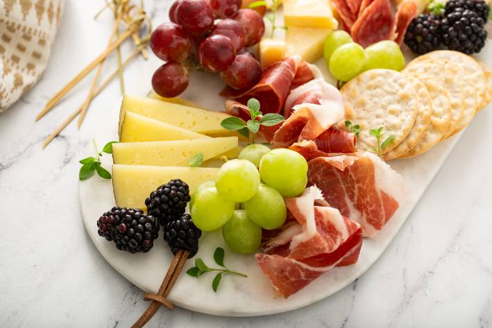 a serving board with fruit, cheese, meat, and crackers