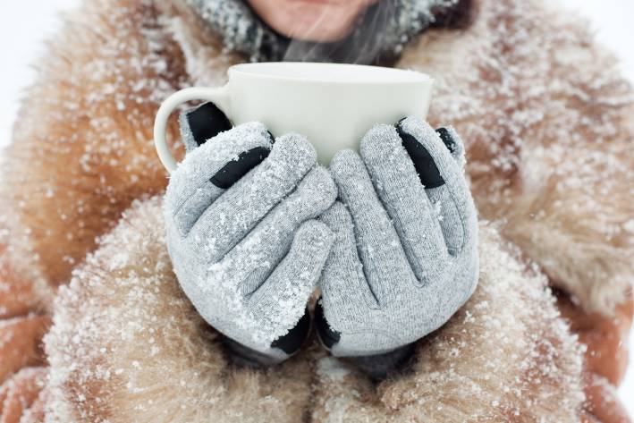 a young woman holding a steaming mug with winter gloves