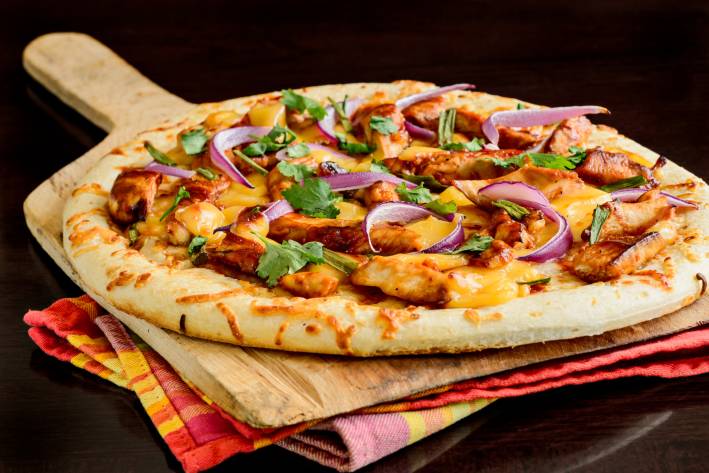 Grilled pizza with meat and purple onions on top of colorful cloths.