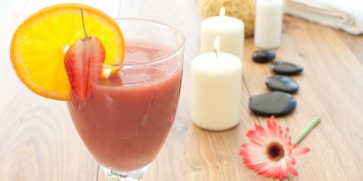 Strawberry smoothie next to candles and a flower 