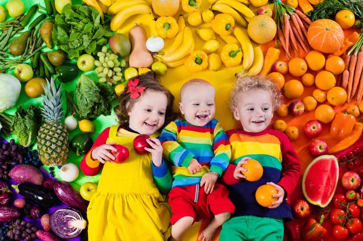 Young cute siblings surrounded by a rainbow of healthy produce