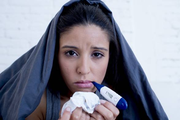 a woman with a cold or the flu, holding tissues and a thermometer