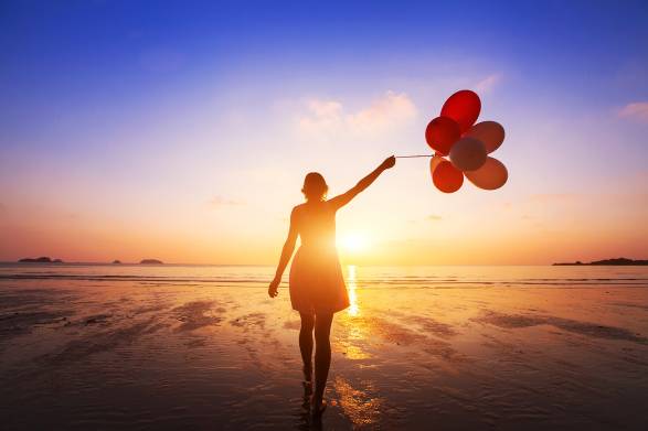 a happy woman holding balloons on the beach at sunset