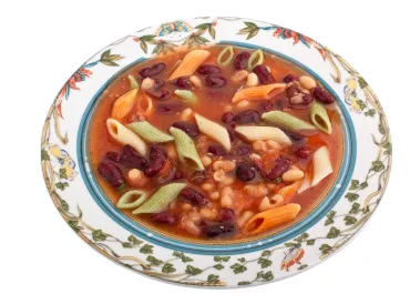 Colorful bowl of minestrone soup in a white bowl with floral decorative elements on rim.