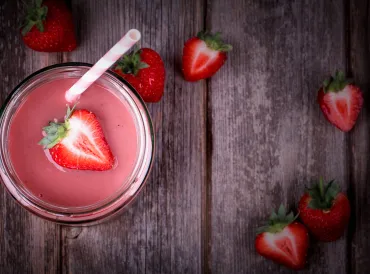 A glass of strawberry smoothie on weathered picnic table wood.
