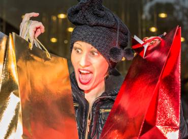 Woman with winter hat on holding up gold and red shopping bags for December holidays..