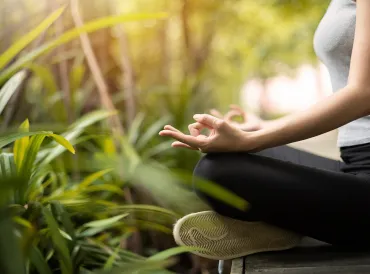 a woman meditating outside, surrounded by plants