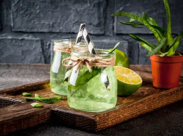 Aloe infused Lime water in drinking jars with black and white paper straws on a cutting board.