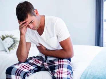 A man sitting on his bed with stomach discomfort.