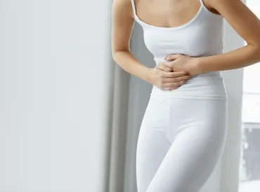 A woman in all white holding her stomach in pain.