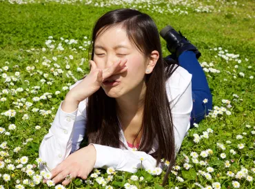 a young Asian girl sneezing in a field of clover
