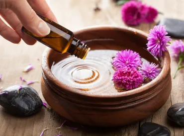 Essential oil being dripped in to a wooden dish for aromatherapy.