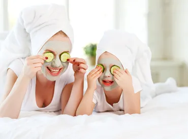 Mother and child with natural face masks on, covering eyes with cucumber slices.