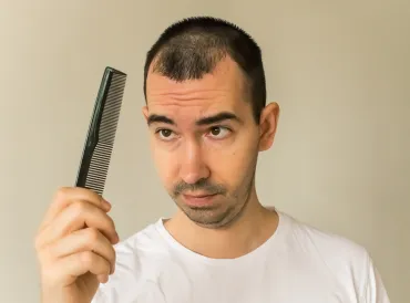 a middle-aged man looking at his comb with worry