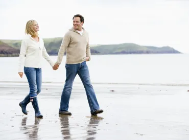a middle-aged couple holding hands while they walk down a rugged beach