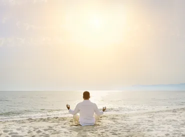 A man meditating on the beach facing a calm sea