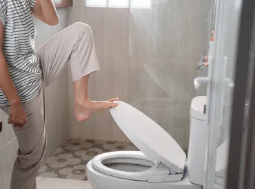 a woman holding her nose and closing the toilet lid with her feet