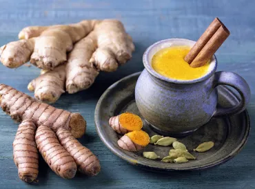 A mug of Golden Milk with turmeric and ginger root beside it.