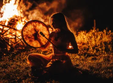 a shamanic woman beating a drum by the fire