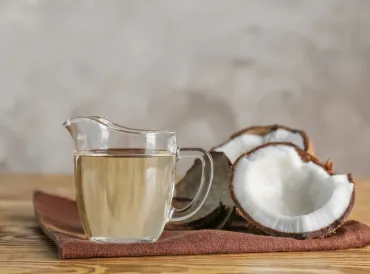 Ripe coconut and pitcher with MCT oil on a wooden table.