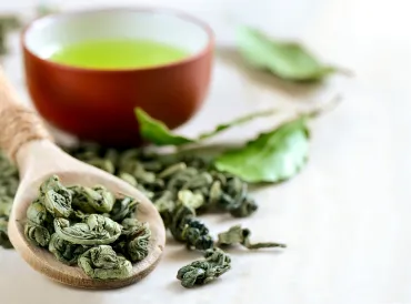 A spoon of dried leaves and a cup of green tea