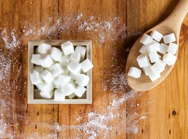 Sugar cubes in a box next to a wooden spoon filled with sugar cubes.