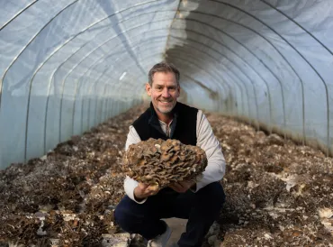 Man in a greenhouse holding up Maitake mushroom.