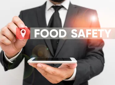 Man in suit holds cell phone flat in one hand and with other is pointing to the words Food Safety
