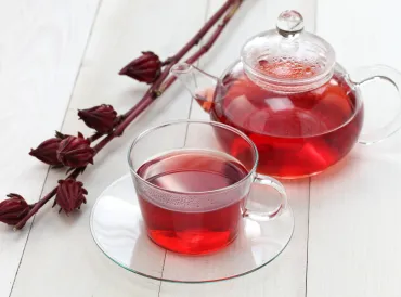 Hibiscus tea in a glass cup in front of a glass tea kettle. 